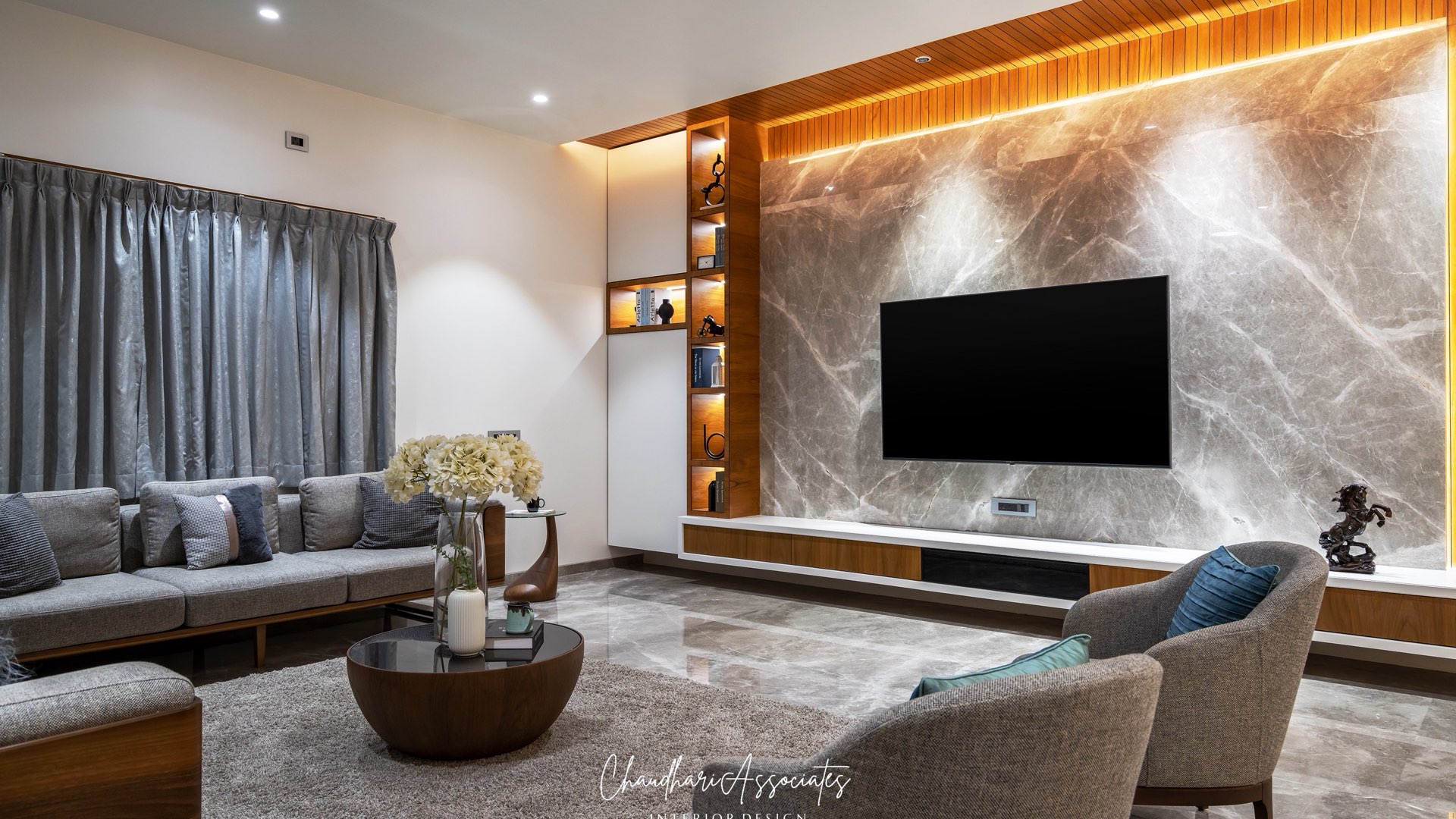 Living room with a backlit marble TV wall, timber ceiling band and tub armchairs — Gajlakshmi, Shirur